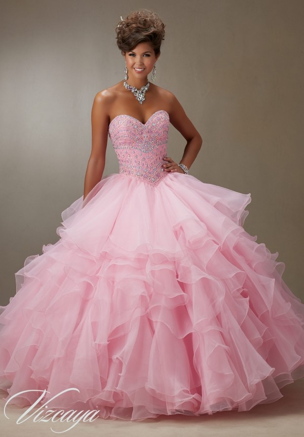 A woman in a pink dress posing for a picture with ruffled Quinceañera dresses